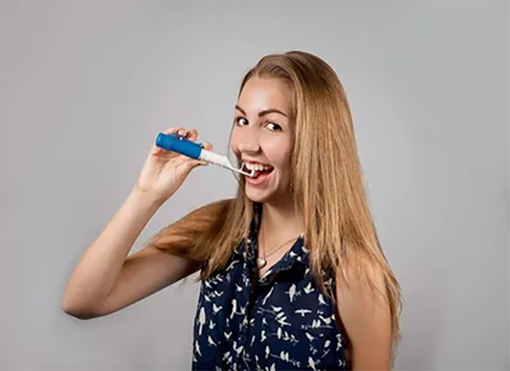 A woman brushing her teeth with an electric toothbrush.